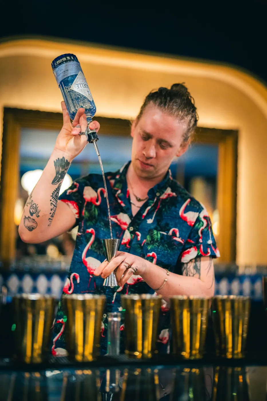 Bartender en chemise à flamants roses qui mesure un spiritueux