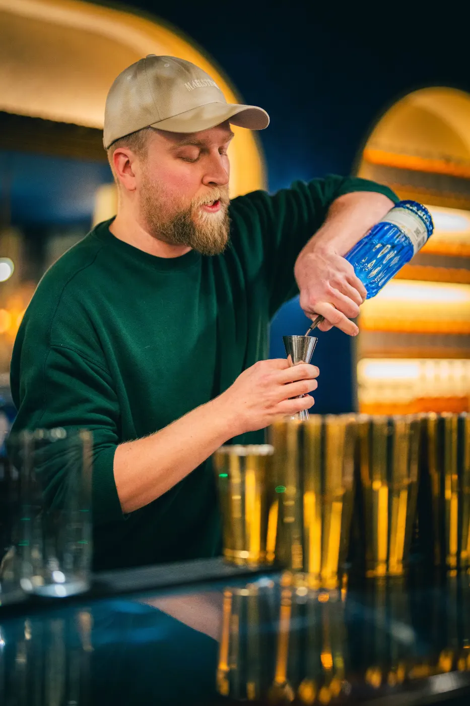 Bartender à casquette qui mesure un spiritueux au jigger